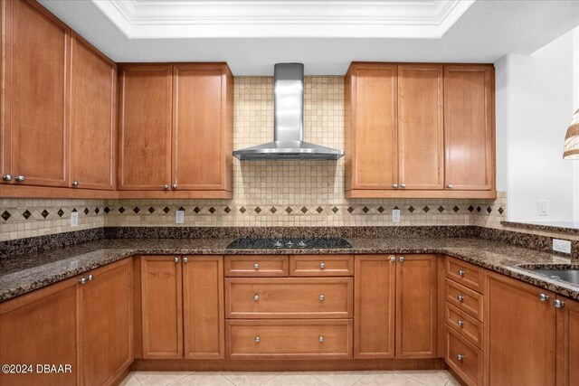 kitchen with black electric cooktop, wall chimney exhaust hood, dark stone countertops, and tasteful backsplash