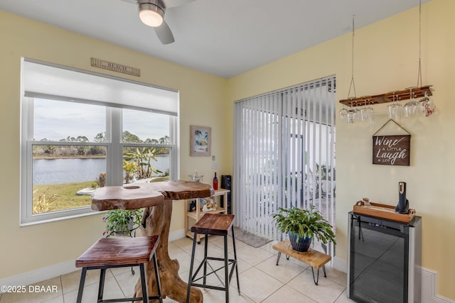 dining area featuring a water view, ceiling fan, and light tile patterned flooring