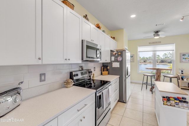 kitchen featuring light tile patterned floors, ceiling fan, appliances with stainless steel finishes, tasteful backsplash, and white cabinets