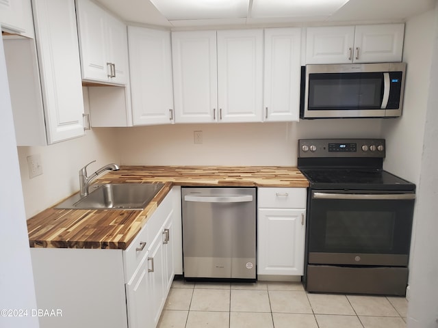 kitchen with stainless steel appliances, white cabinetry, sink, and wooden counters