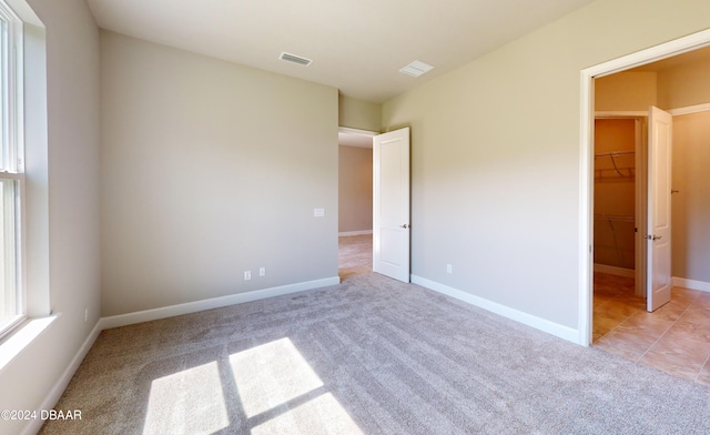 unfurnished bedroom with light carpet, a closet, and a walk in closet