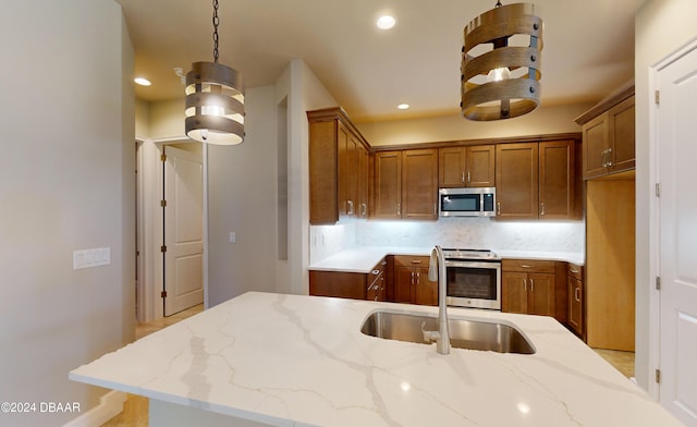 kitchen featuring light stone counters, stainless steel appliances, hanging light fixtures, decorative backsplash, and sink