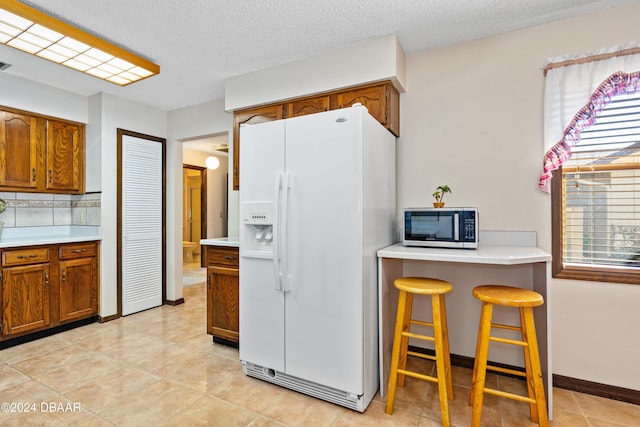 kitchen with backsplash, white fridge with ice dispenser, a textured ceiling, light tile patterned flooring, and a breakfast bar area