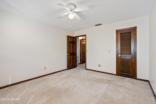 unfurnished bedroom featuring ceiling fan, light colored carpet, and a textured ceiling