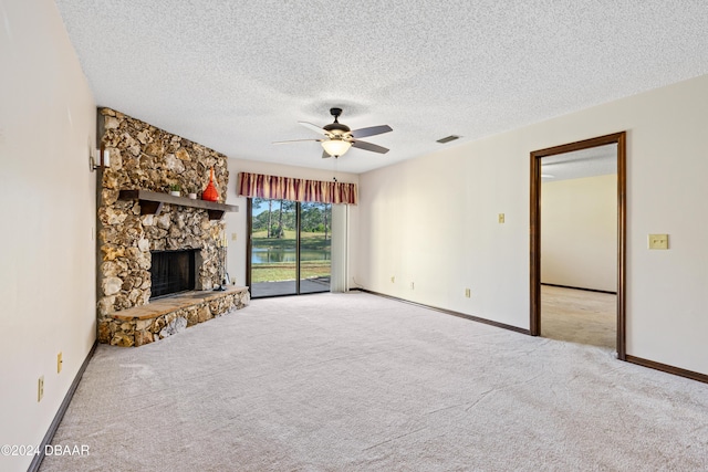 unfurnished living room featuring a textured ceiling, light colored carpet, a stone fireplace, and ceiling fan