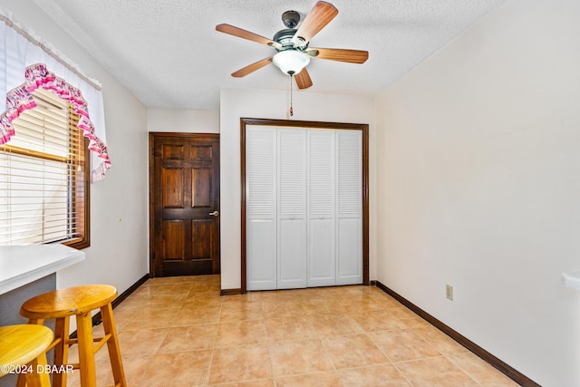 unfurnished bedroom with light tile patterned flooring, a textured ceiling, a closet, and ceiling fan