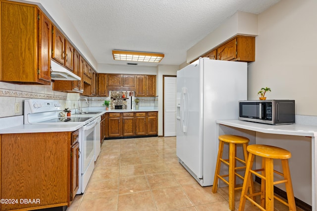 kitchen featuring white appliances, backsplash, sink, a textured ceiling, and a kitchen bar