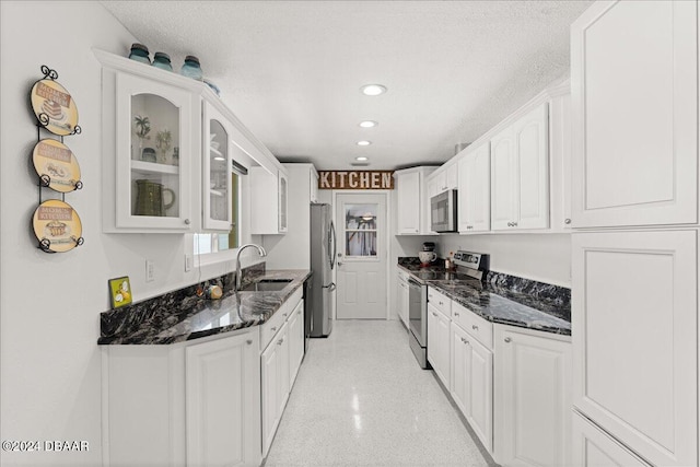 kitchen with stainless steel appliances, dark stone counters, sink, and a textured ceiling