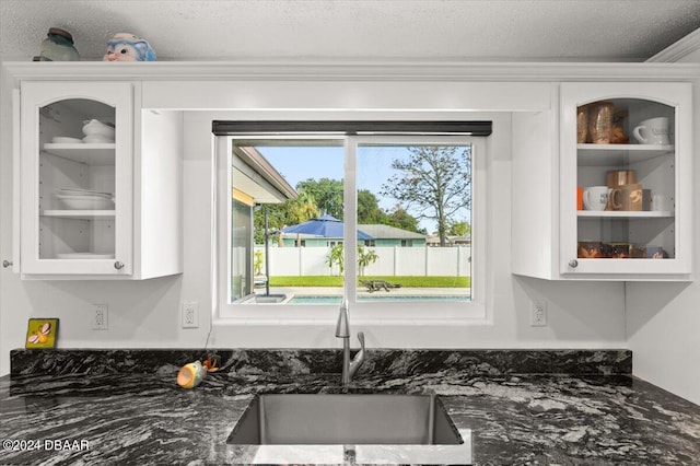 interior details featuring dark stone counters, white cabinetry, sink, and a textured ceiling