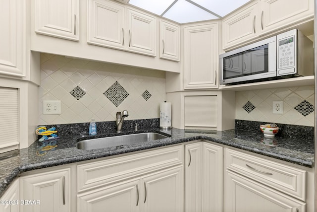 kitchen with backsplash, white cabinetry, stainless steel microwave, and sink