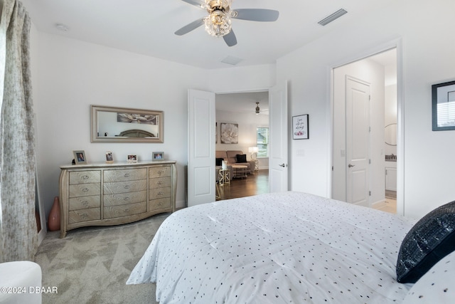 bedroom featuring ceiling fan, light colored carpet, and ensuite bath