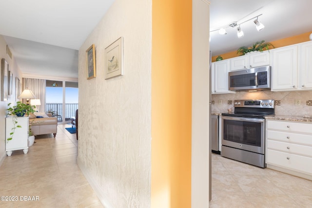 kitchen featuring light tile patterned flooring, appliances with stainless steel finishes, light stone countertops, decorative backsplash, and white cabinets