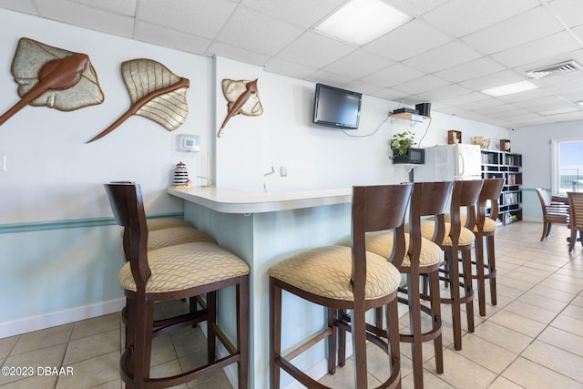 bar featuring a paneled ceiling and light tile patterned floors