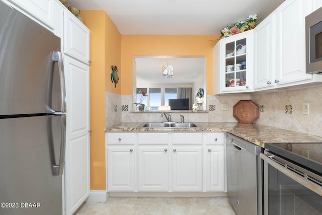 kitchen with stainless steel appliances, white cabinetry, sink, light stone counters, and backsplash