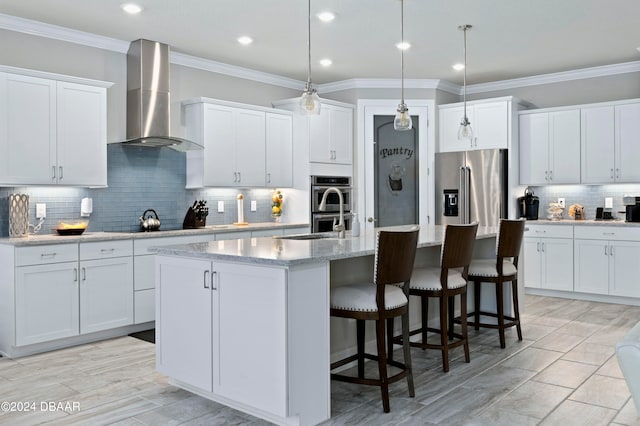 kitchen featuring white cabinetry, an island with sink, stainless steel appliances, and wall chimney range hood