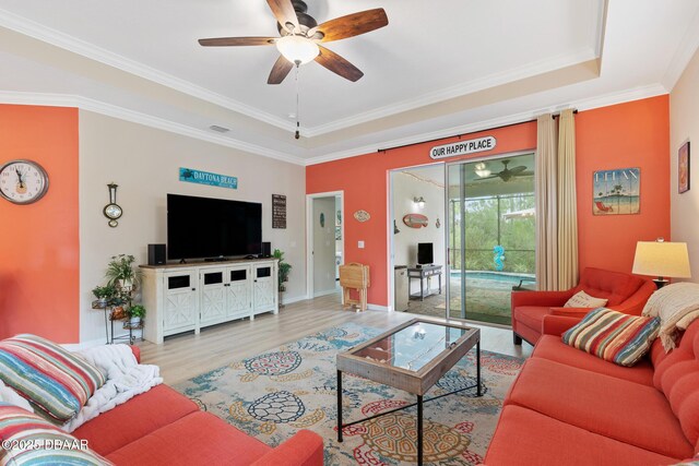 living room featuring ceiling fan with notable chandelier, wood-type flooring, crown molding, and a tray ceiling