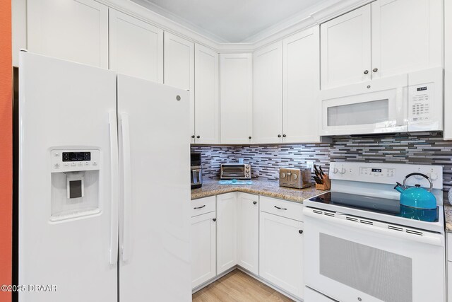 kitchen with light hardwood / wood-style floors, white cabinetry, light stone counters, ornamental molding, and white appliances