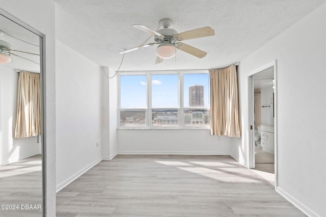 unfurnished bedroom with a textured ceiling, ensuite bath, light hardwood / wood-style flooring, and ceiling fan