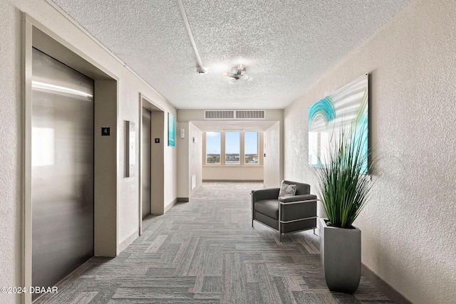 hallway with elevator, carpet floors, and a textured ceiling