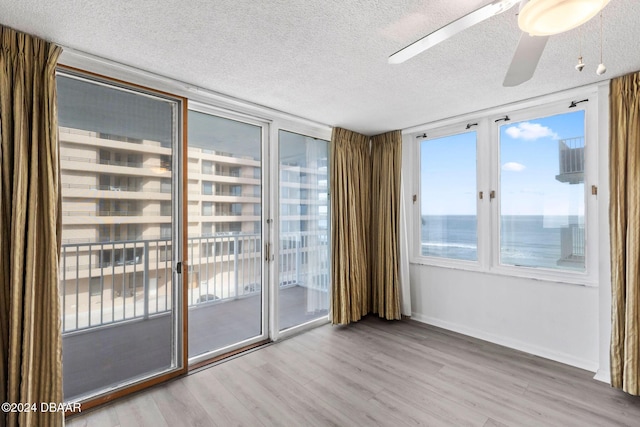 spare room with ceiling fan, a water view, a textured ceiling, and light hardwood / wood-style flooring