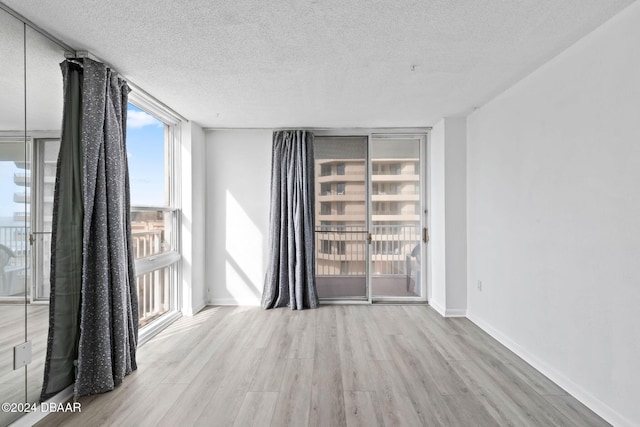 unfurnished room featuring light hardwood / wood-style flooring, a textured ceiling, and a wall of windows