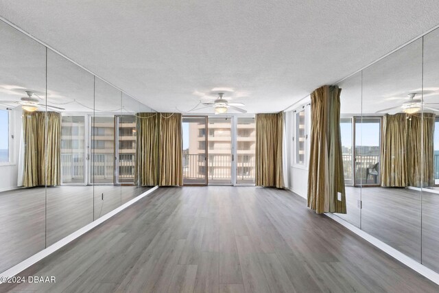 empty room featuring hardwood / wood-style flooring, ceiling fan, a wall of windows, and a textured ceiling