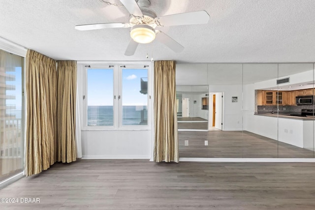 unfurnished living room with a water view, sink, ceiling fan, a textured ceiling, and wood-type flooring