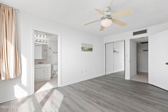 unfurnished bedroom with ensuite bath, ceiling fan, a closet, and wood-type flooring