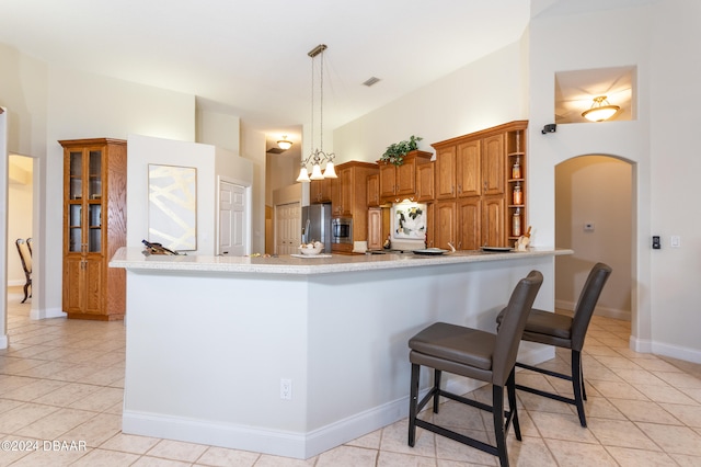 kitchen with kitchen peninsula, hanging light fixtures, light tile patterned floors, a breakfast bar, and stainless steel refrigerator