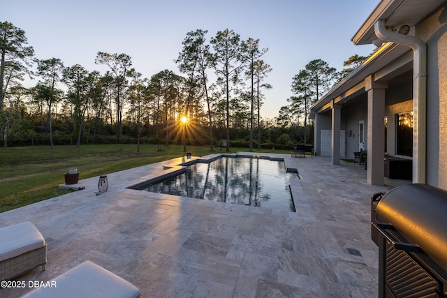 pool at dusk featuring a patio area, grilling area, and a yard