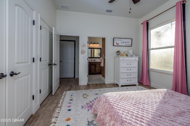 bedroom featuring light wood-type flooring, multiple windows, ceiling fan, and connected bathroom