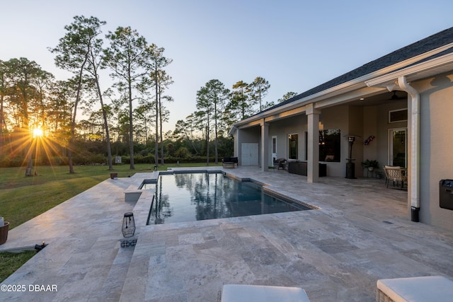 pool at dusk featuring a patio and a lawn