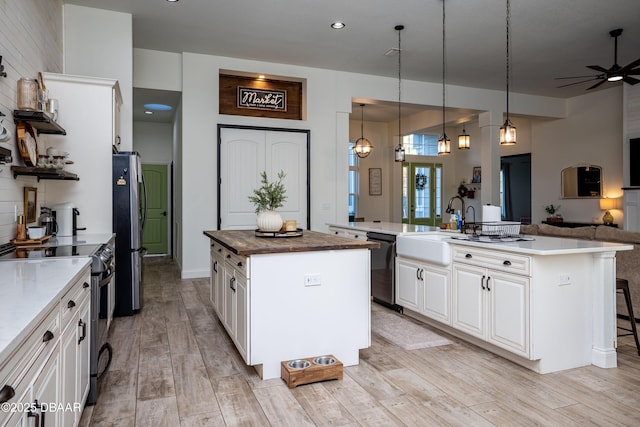 kitchen with a center island with sink, stainless steel appliances, white cabinets, decorative light fixtures, and ceiling fan with notable chandelier