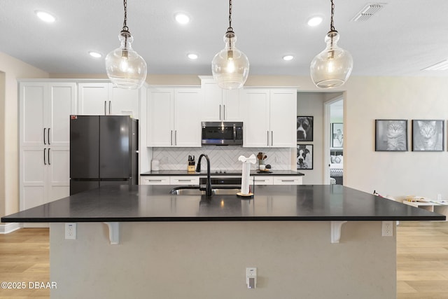 1602 Killian Drive Ne, Palm Bay, FL 32905 - kitchen with stainless steel microwave, freestanding refrigerator, dark countertops, light wood-style floors, and a kitchen island with sink