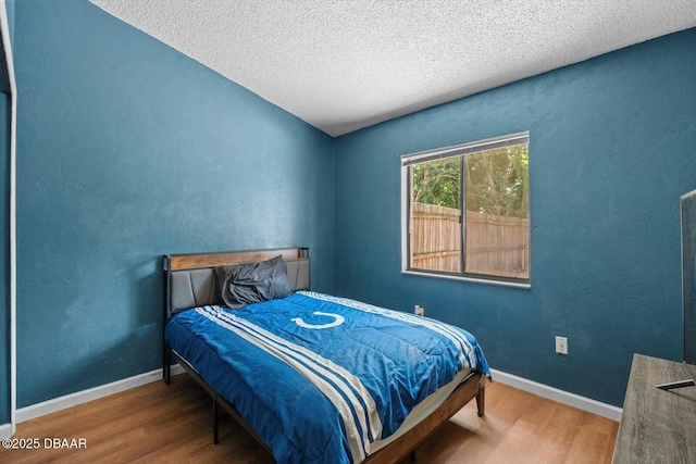 bedroom featuring baseboards, wood finished floors, and a textured ceiling