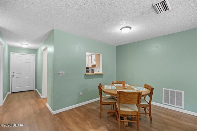 dining area with visible vents, a textured ceiling, and wood finished floors