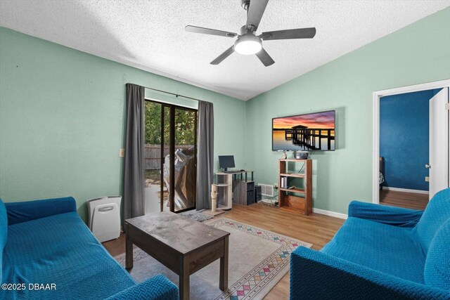 living area with baseboards, vaulted ceiling, a textured ceiling, ceiling fan, and wood finished floors