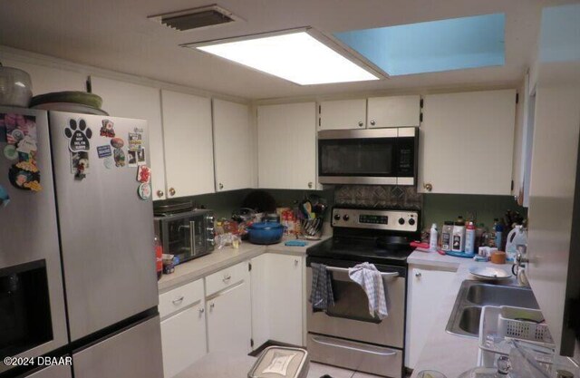 kitchen with appliances with stainless steel finishes, light tile patterned floors, sink, white cabinets, and a skylight