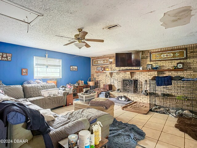 living room with a textured ceiling, light tile patterned floors, ceiling fan, and a brick fireplace