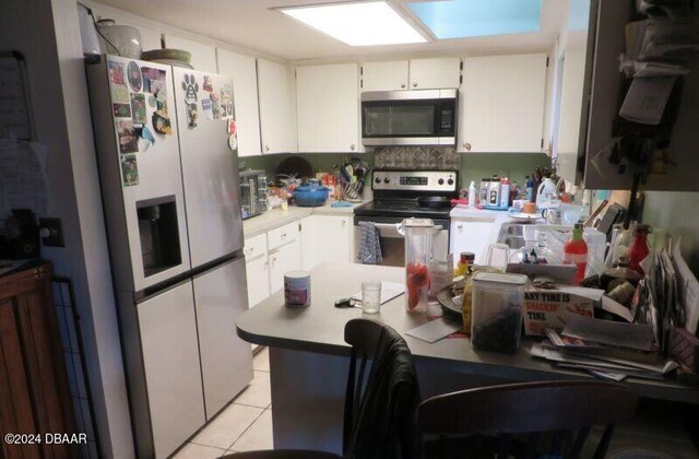 kitchen with a skylight, white cabinets, light tile patterned flooring, and stainless steel appliances