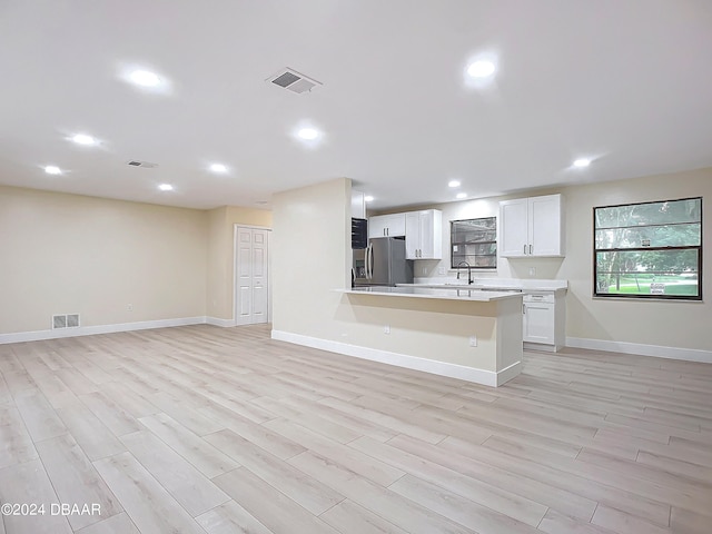 kitchen featuring stainless steel fridge, white cabinetry, light wood-type flooring, and a breakfast bar