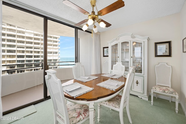 dining space featuring a water view, a textured ceiling, carpet, and ceiling fan