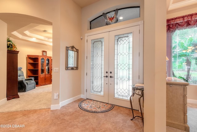 entrance foyer with light colored carpet, ornamental molding, a tray ceiling, and french doors