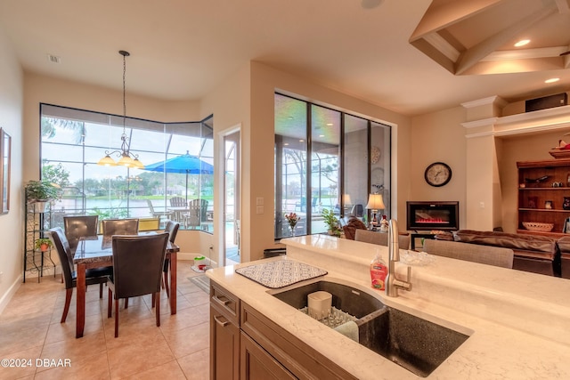 kitchen with light stone countertops, sink, light tile patterned floors, a chandelier, and hanging light fixtures