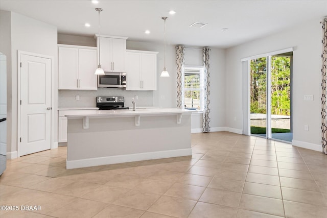 kitchen with a healthy amount of sunlight, a kitchen island with sink, light countertops, appliances with stainless steel finishes, and backsplash