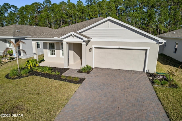 ranch-style home with a front yard, an attached garage, a shingled roof, stucco siding, and decorative driveway