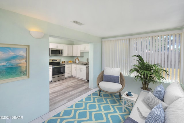 interior space featuring stainless steel appliances, light hardwood / wood-style floors, white cabinetry, and sink