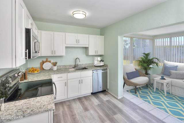 kitchen featuring stainless steel appliances, white cabinetry, sink, light stone counters, and light wood-type flooring