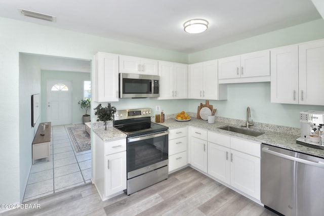 kitchen featuring stainless steel appliances, sink, light stone countertops, white cabinets, and light wood-type flooring