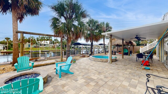 view of patio / terrace with an outdoor fire pit, an in ground hot tub, ceiling fan, and a water view